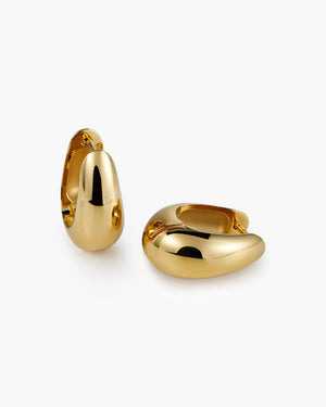 Pair of chunky gold huggie hoop earrings with a rounded, domed design, laid on a white background.