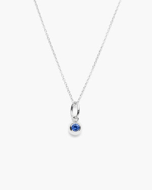 Close-up of silver necklace with a dangling blue pendant against a white background