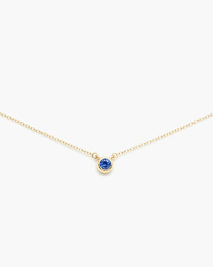 Gold cable chain necklace with a small round blue gemstone pendant centered on a white background
