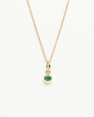 Gold cable chain necklace with a small round green gemstone pendant hanging from a gold bail on a white background