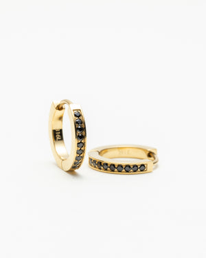 Pair of gold huggie hoop earrings set with a row of black gemstones, laid on a white background.