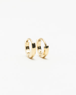 Pair of small gold huggie hoop earrings engraved "LUAH" on the inner band, laid on a white background.