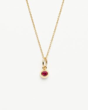 Gold cable chain necklace with a small round red gemstone pendant hanging from a gold bail on a white background