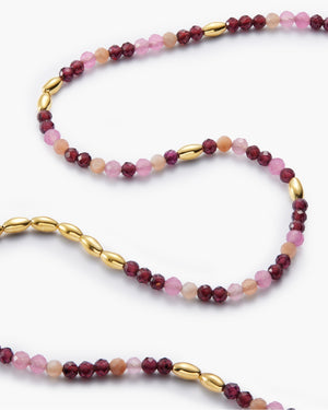Close up of gold beaded necklace with pink and burgundy stone accents on white background