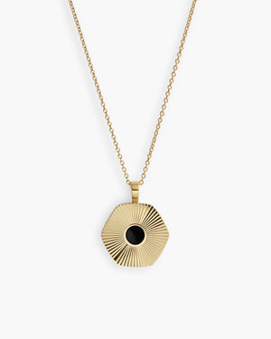 Gold chain necklace with a hexagonal  pendant featuring a round black stone center, photographed on a plain white background.