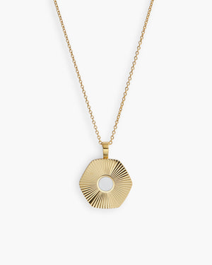 Close-up of gold hexagonal necklace with a ribbed detail and white centre, against a white background 