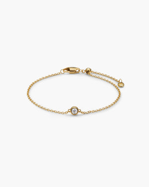 Delicate gold chain bracelet with a single gemstone charm, lobster clasp, and extender chain, laid flat on a white background.
