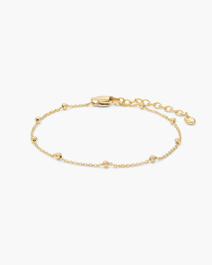 Gold chain bracelet with small ball bead accents, lobster clasp, and extender chain, laid flat on a white background.