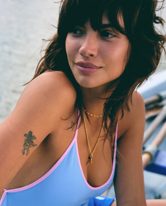 Woman wearing layered gold necklaces with a bar pendant, and a light blue top