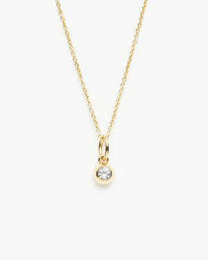 Close-up of gold necklace with a dangling white sapphire pendant against a white background