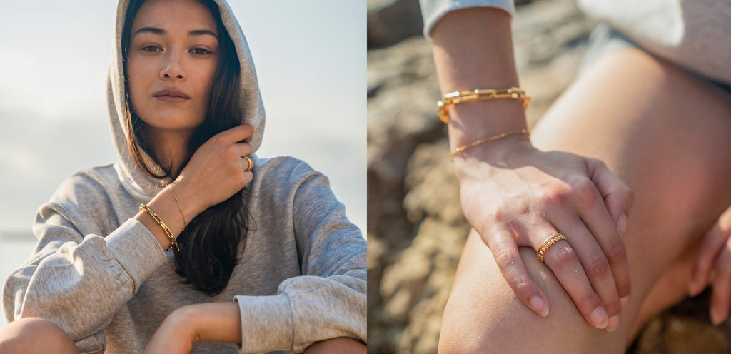 Woman in a hoodie on a beach with close-up of hands wearing gold bracelets and a ring.